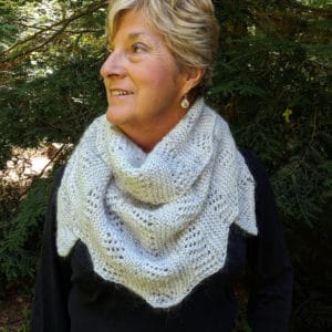 Smiling woman with short blonde hair modeling an asymmetrical, triangular light gray wrap featuring a lace motif. She is wearing it bandana style.